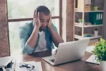 Man sitting at a laptop holding his head in his hands
